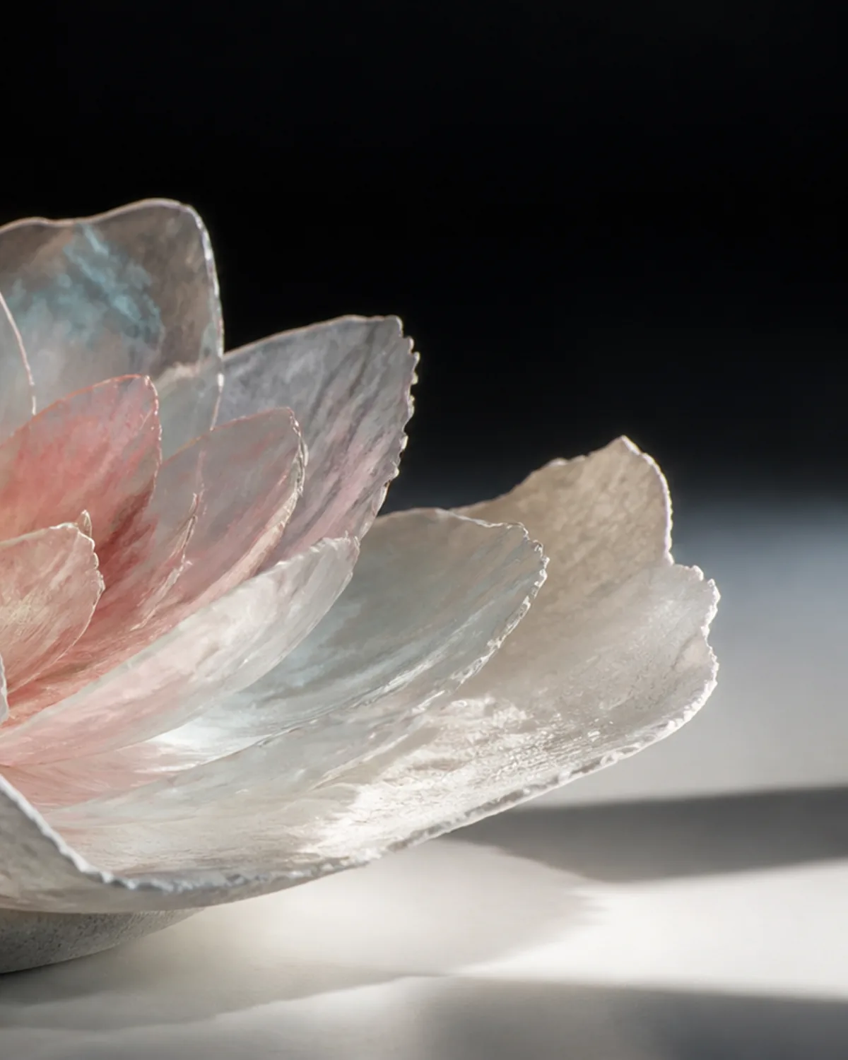 A translucent flower with paper petals and a glass center on a warm studio surface.