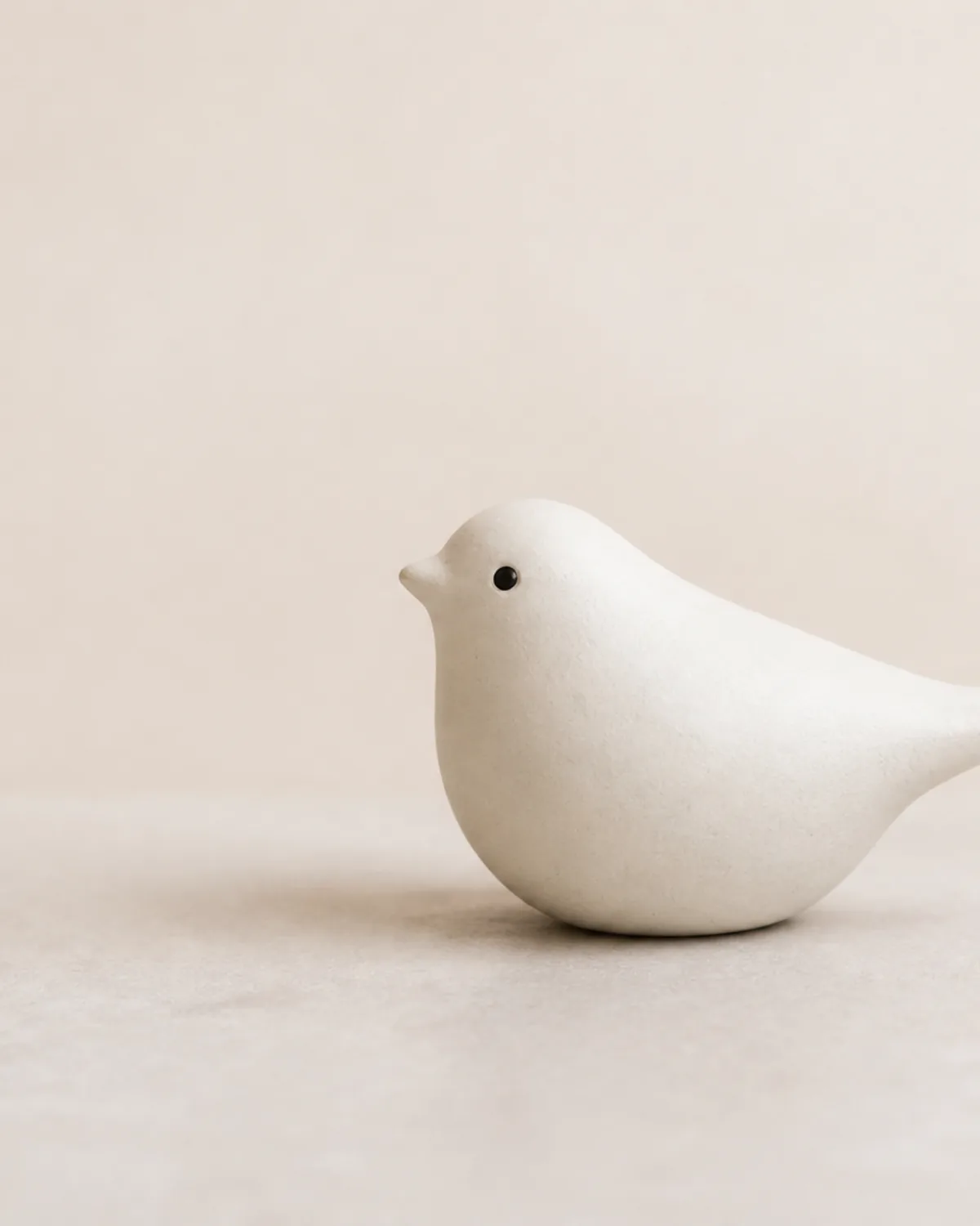 A matte white ceramic bird sculpture on a softly lit neutral pedestal.