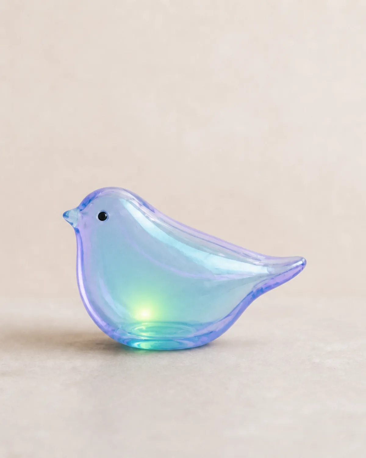 A translucent glass bird glowing with cyan and violet light on a dark pedestal.